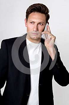 Elegant, young man in a business suit, standing on a white background and talking on a mobile phone