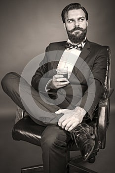 elegant young man with retro look sitting in an armchair and holding a glass of whiskey