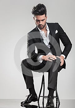 Elegant young man stitting on a stool while looking down
