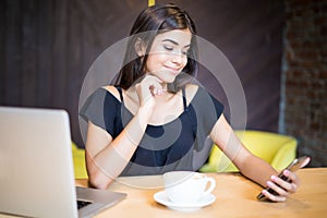 Elegant young smile woman with a laptop computer at a cafe using a mobile phone .