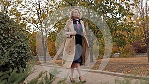 An elegant young woman in a beige coat and dress walks in an autumn Park.