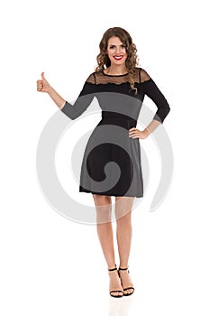 Elegant Young Woman In Black Cocktail Mini Dress And High Heels Is Showing Thumb Up And Smiling