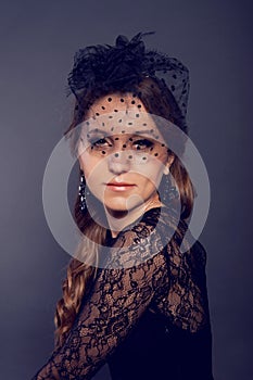 Elegant young woman in black lace dress and veil hat with long c