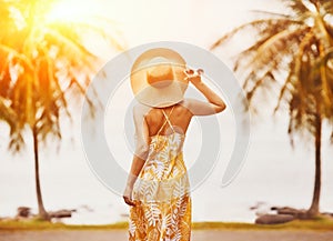 Elegant young woman in dress and hat on beach