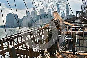 Elegant young woman dressed in fashionable jumpsuit standing on the Brooklyn Bridge.