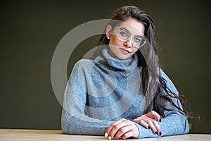Elegant young woman in glasses and a gray sweater on a dark background with a copy space