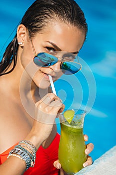 Elegant young woman in the pool with a cocktail.