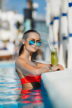 Elegant young woman in the pool with a cocktail.