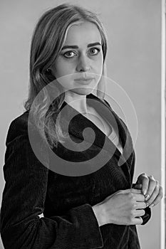 Elegant young woman posing leaning against a white wall. Woman in a classic jacket against a white wall