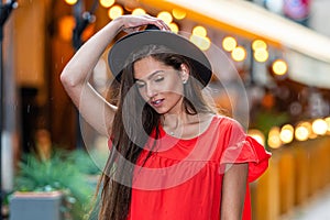 Elegant young woman in a red dress and a black hat on a background of street cafe lights