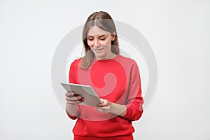 Elegant young woman in red sweater using tablet, looking at screen