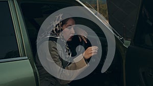 An elegant young woman sits gracefully in her vintage car, the door invitingly open