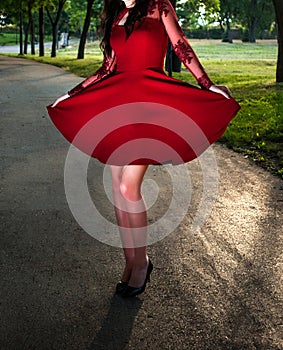 Elegant Young Woman in Striking Red Dress Posing in a Green Park at Sunset