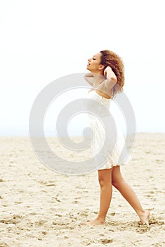 Elegant young woman walking on sand with hands in hair