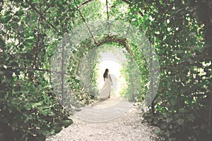 elegant young woman walks happily towards the exit of a tunnel formed by lush plants