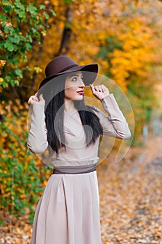 Elegant young woman in wide-brimmed hat gracefully poses with poise in scenic autumn park