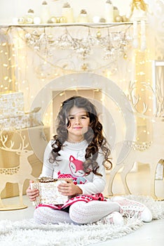 Elegantly dressed adorable curly girl with delight admires gold Christmas garlands magic lights and tree decorations