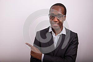 Elegantly dressed african businessman wears eyeglasses and points his finger to left. Advertising concept