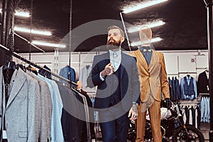 Elegantly dressed bearded shop assistant with standing near mannequin in menswear store.