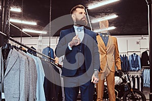 Elegantly dressed bearded shop assistant with standing near mannequin in menswear store.