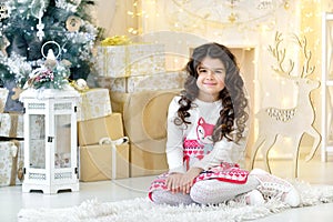 Elegantly dressed curly girl with delight admires gold Christmas garlands magic lights and tree decorations