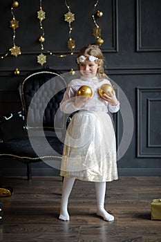 Elegantly dressed girl of 8-9 years plays Christmas-tree decorations.