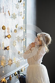 Elegantly dressed girl with delight admires gold Christmas-tree decorations.