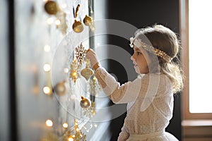 Elegantly dressed girl of 8-9 years with delight touches gold Christmas garlands
