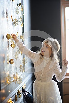 Elegantly dressed girl of 8-9 years with delight touches gold Christmas garlands