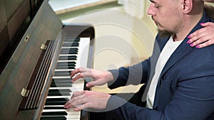 An elegantly dressed man plays a song on the piano.