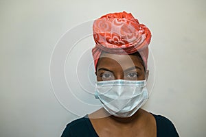 An elegantly dressed young African woman wearing a headscarf at home and a medical mask. Pandemic concept