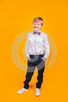 Elegantly dressed young blonde boy posing and smiling on yellow background
