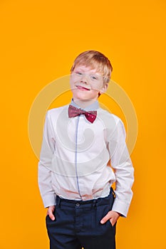 Elegantly dressed young blonde boy posing and smiling on yellow background