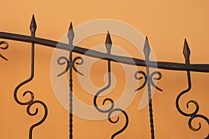 Element of a forged brown metal fence, gate on the background of a wall