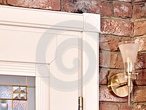 Element of white wooden interior carved door with classic geometric ornament stained glass and a lamp on brick wall background