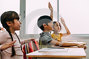 Elemental edad asiático alumno chico elevado manos arriba en A la clase. diverso grupo de alumnos en elemental 