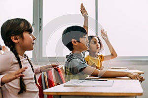 Elementary age Asian student boy raised hands up in Q and A classroom. Diverse group of pre-school pupils in elementary