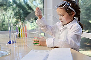 Elementary age girl, little chemist using glass laboratory pipette, picking up green solution from a flat-bottomed flask