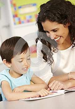 Elementary Age Schoolgirl Reading Book In Class With Teacher