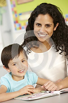 Elementary Age Schoolgirl Reading Book In Class With Teacher