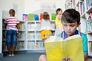 Elementary boy reading book at school library