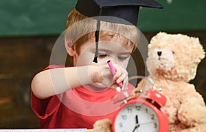 Elementary education concept. First former with toy on desk, close up. Pupil in mortarboard, chalkboard on background