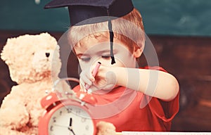 Elementary education concept. First former with toy on desk, close up. Pupil in mortarboard, chalkboard on background