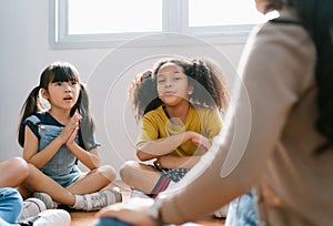 Elementary international students sitting on floor in circle around the teacher and listening a story in their classroom.The