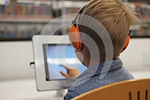 Elementary school boy sitting in library, using touchscreen computer for education