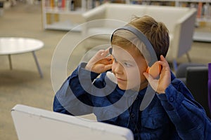 Elementary school boy sitting in library, using touchscreen computer for education
