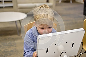 Elementary school boy sitting in library, using touchscreen computer for education