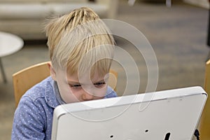 Elementary school boy sitting in library, using touchscreen computer for education