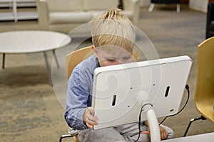 Elementary school boy sitting in library, using touchscreen computer for education