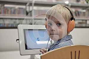 Elementary school boy sitting in library, using touchscreen computer for education
